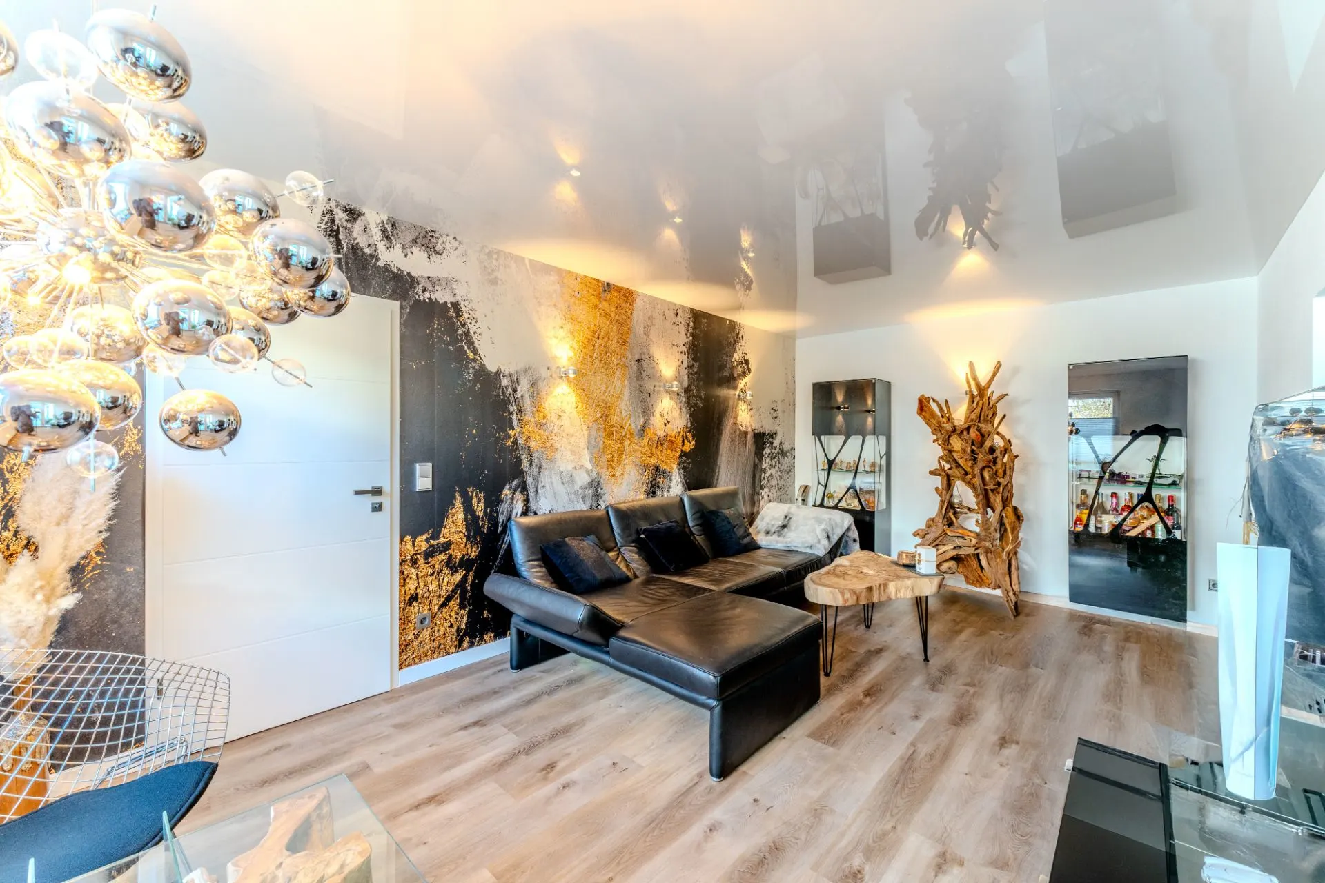 Modernes Wohnzimmer mit schwarzem Sofa, Holzboden, Kunstwand und auffälliger Beleuchtung.