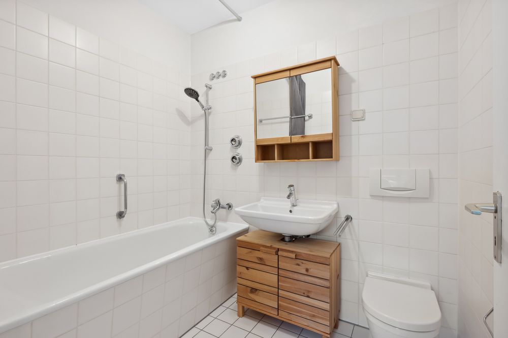 Helles Badezimmer mit Badewanne, Dusche, Waschbecken, Holzschrank und Toilette.