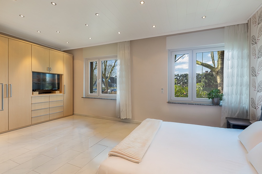 Helles Schlafzimmer mit großem Einbauschrank, Doppelbett und zwei Fenstern mit Blick nach draußen.