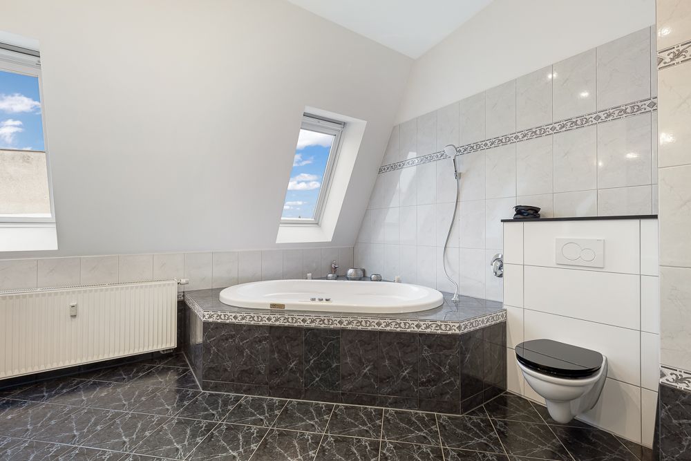 Modernes Badezimmer mit Eckbadewanne, Wandtoilette und zwei Dachfenstern.