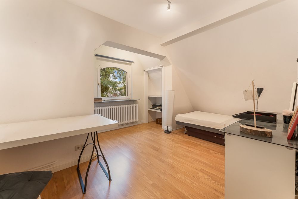 Helles Zimmer mit Holzboden, Schreibtisch, Bett und Fenster mit Blick ins Grüne.