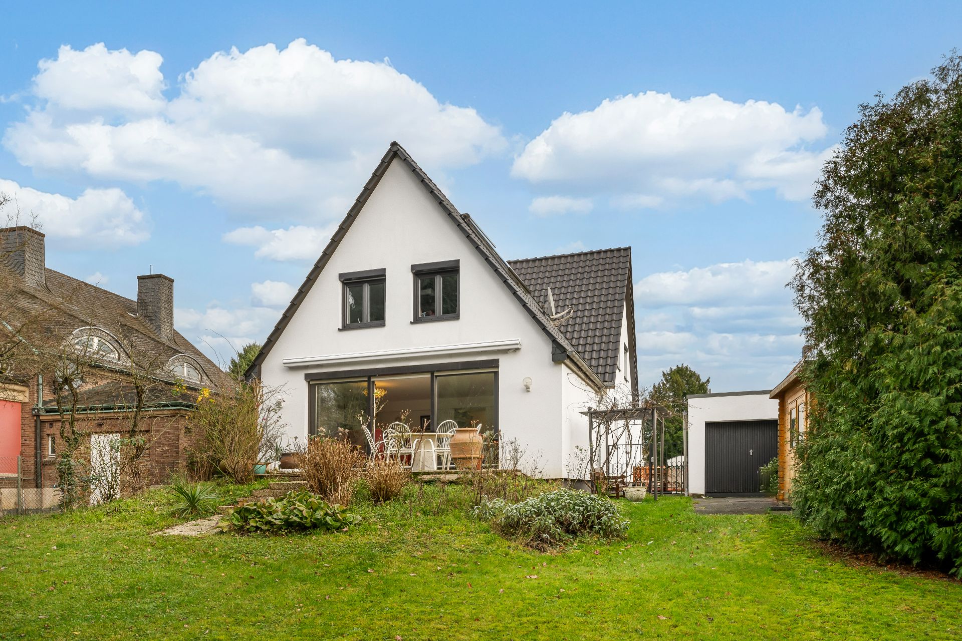 Weiße Einfamilienhaus mit Giebeldach, großem Fenster und Garten im Vordergrund.