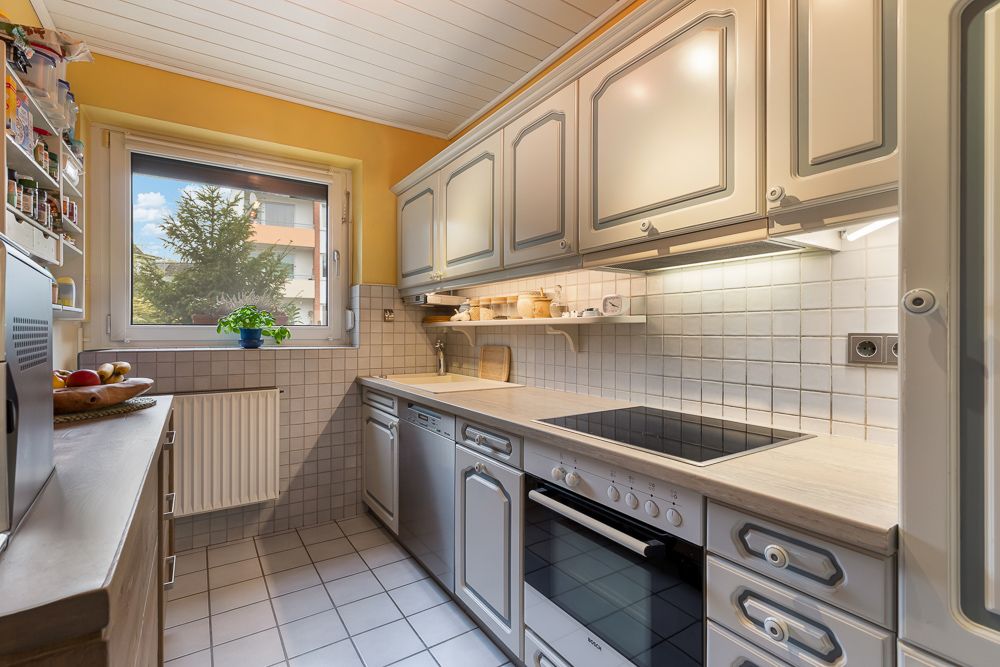 Helle Küche mit weißen Schränken, Herd, Spülmaschine und Fenster mit Blick nach draußen.