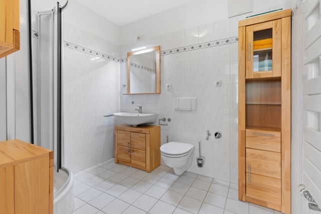 Helles Badezimmer mit Holzschränken, Wand-WC, Waschbecken, Spiegel und Dusche.
