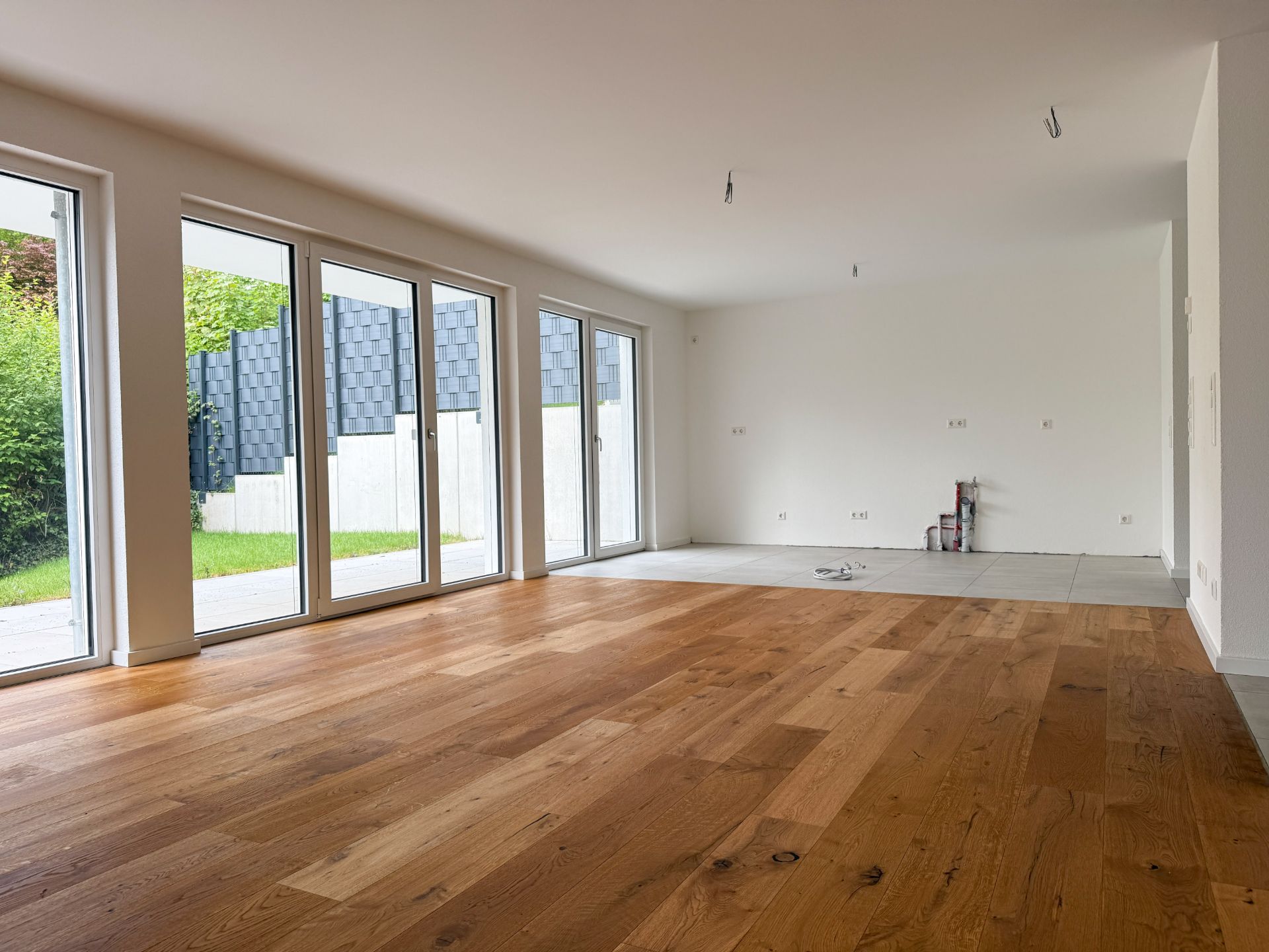 Leerer Raum mit großem Fenster, Holzboden und Zugang zum Garten.