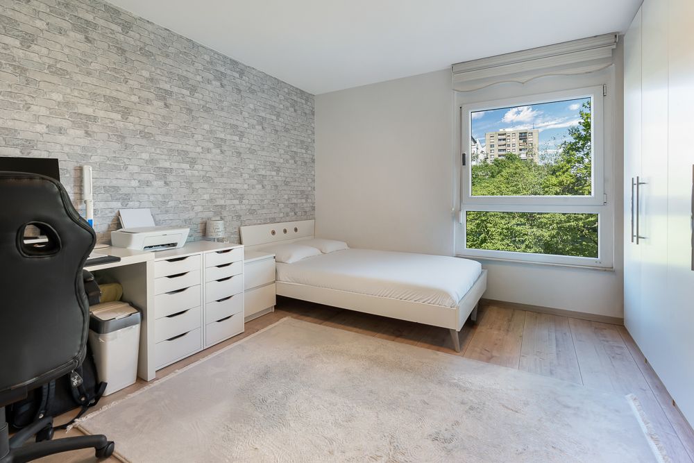 Modernes Schlafzimmer mit Schreibtisch, Stuhl, Doppelbett und großem Fenster mit Ausblick.