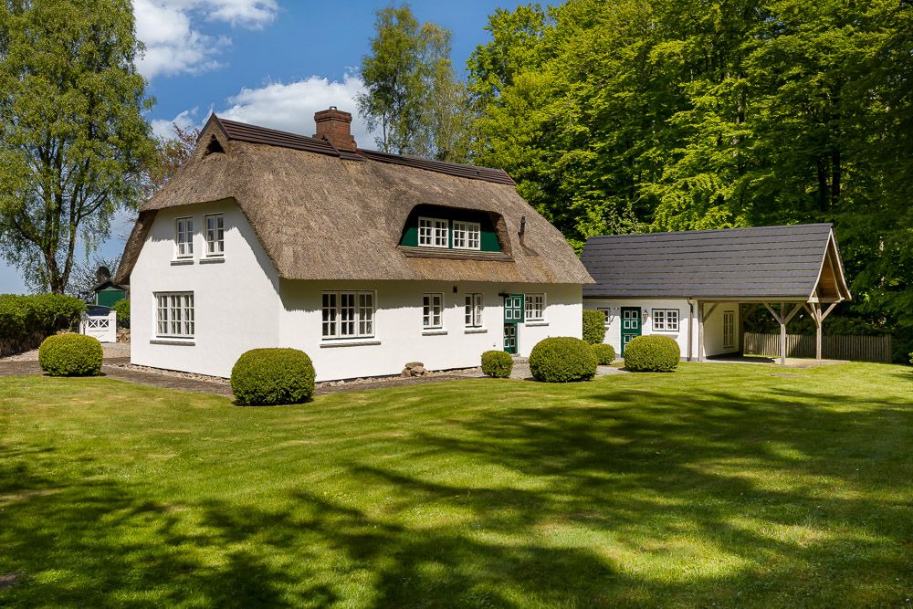 Weißes Reetdachhaus mit grünen Fensterläden und gepflegtem Garten bei sonnigem Wetter.
