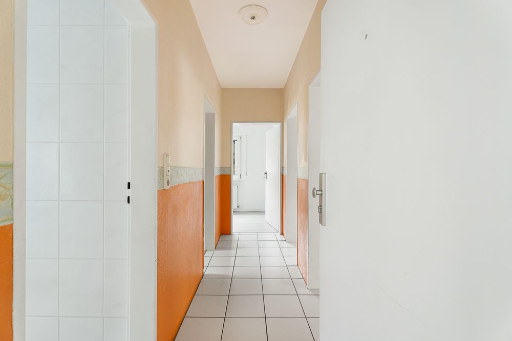 Heller Flur mit weißen Türen und orangefarbenen Wänden, Boden aus weißen Fliesen.