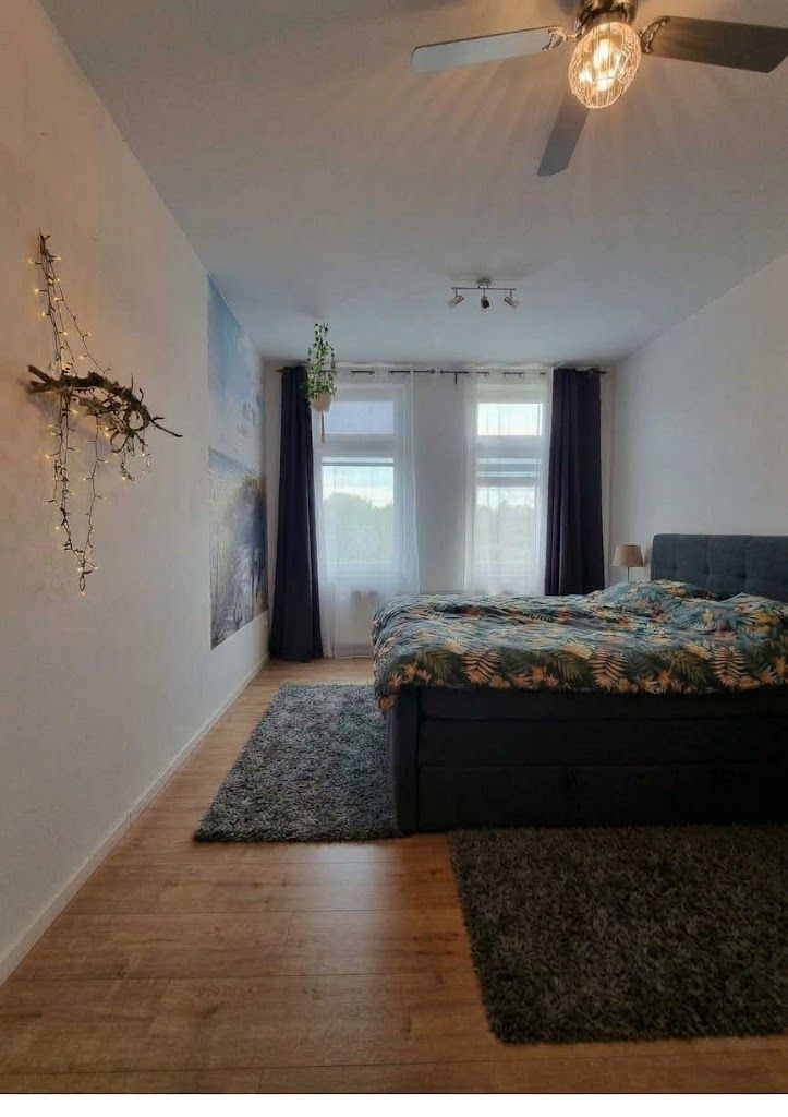 Schlafzimmer mit Doppelbett, Teppichen, Fenster mit Vorhängen und Deckenventilator.