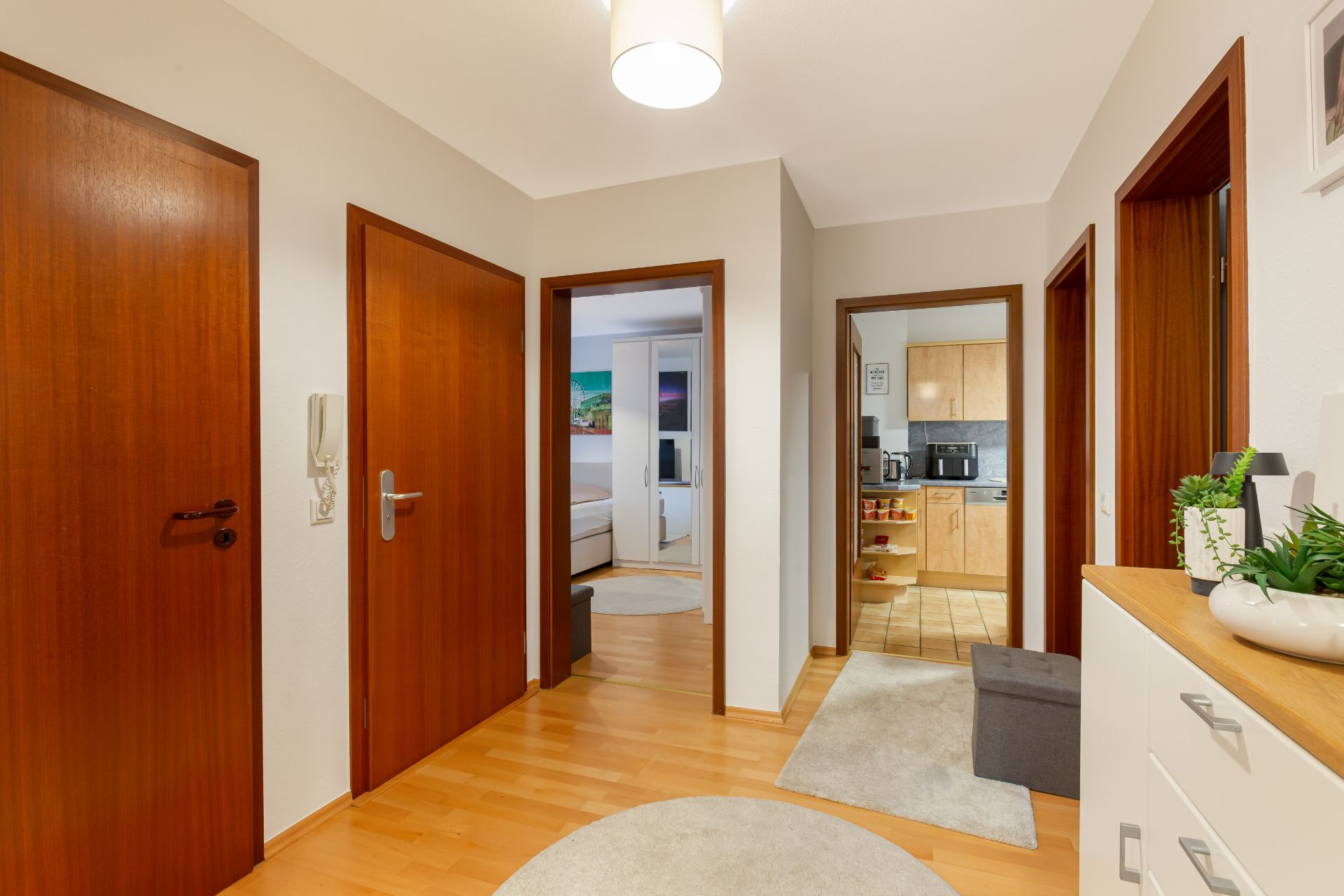 Heller Flur mit Holztüren, hellem Boden und Blick in Schlafzimmer und Küche.
