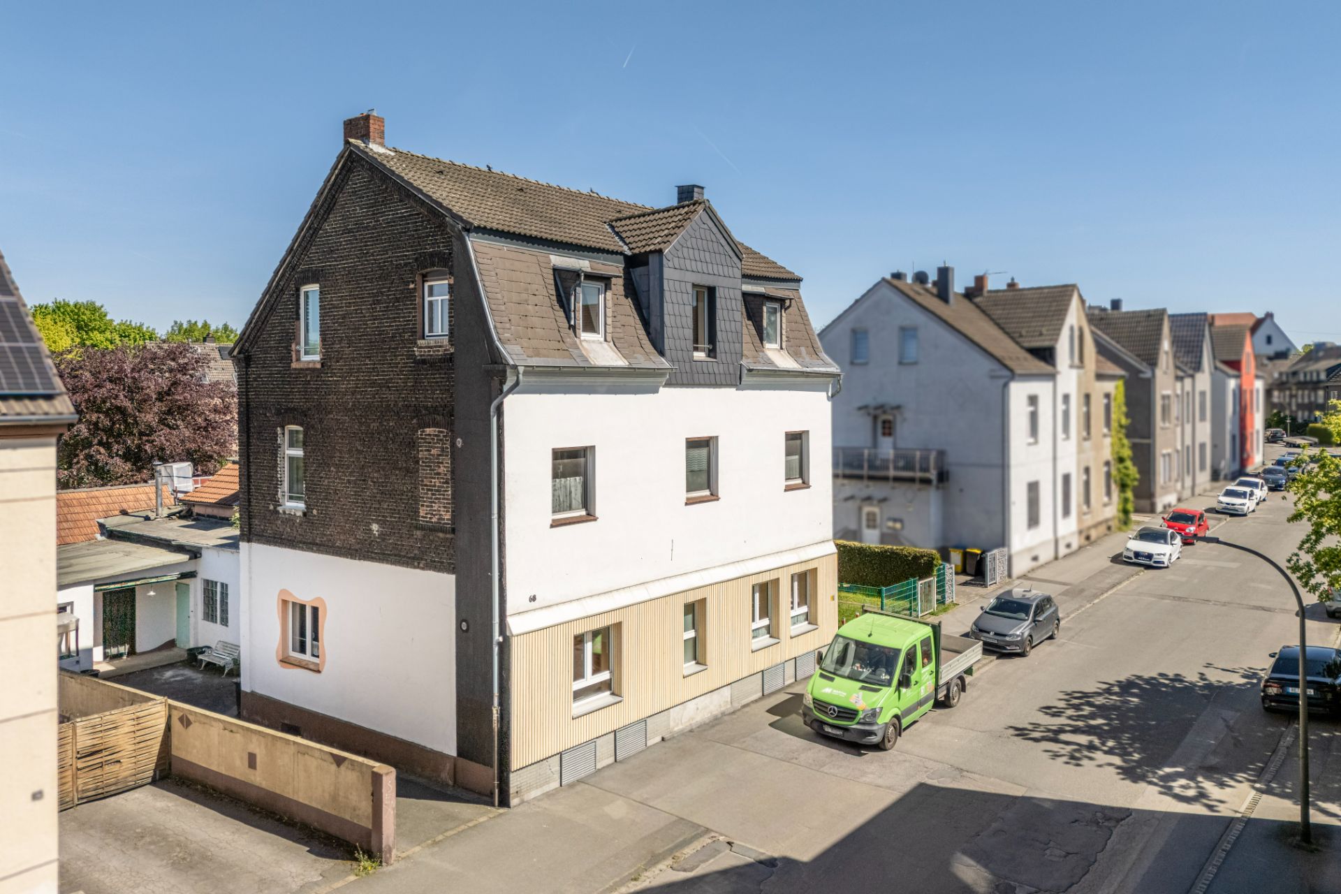 Dreistöckiges Wohnhaus an einer ruhigen Straße mit geparkten Autos und klarem Himmel.