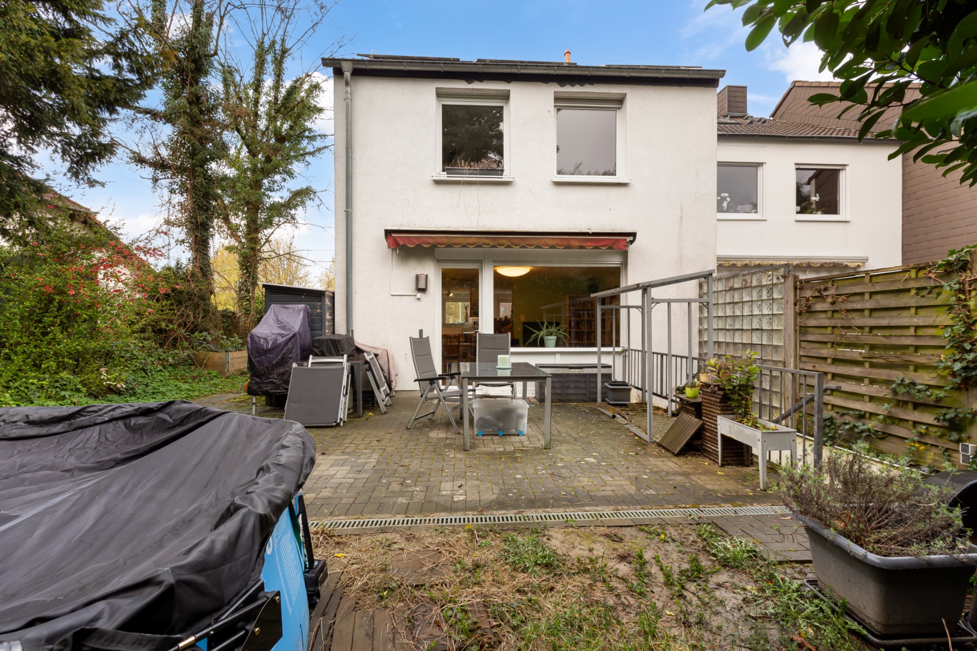 Hinterhof eines Wohnhauses mit Terrasse, Tisch, Stühlen und Gartenmöbeln.