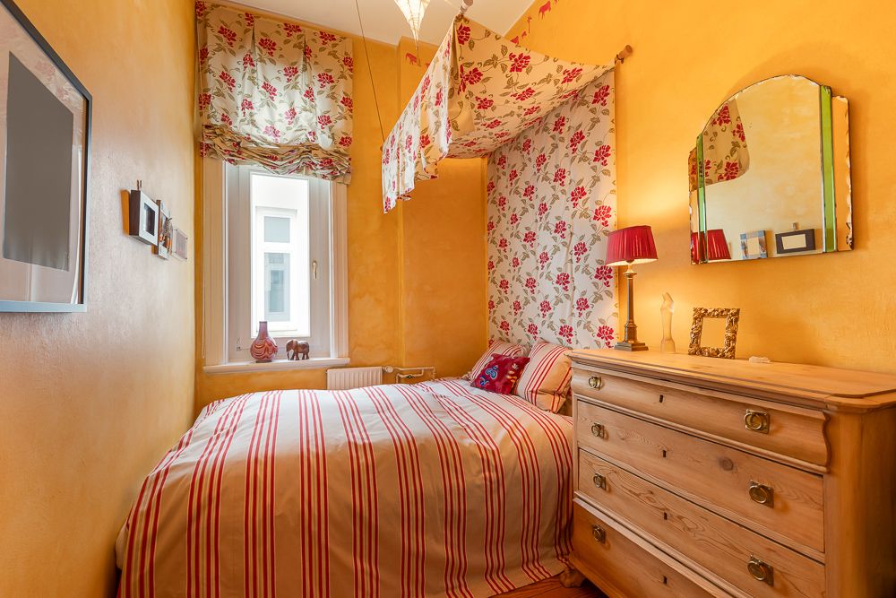 Kleines Schlafzimmer mit gelben Wänden, Einzelbett, Kommode und Blumenmustern.