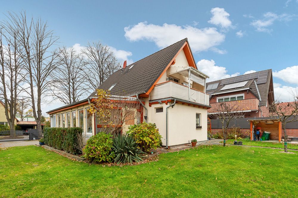 Wohnhaus mit Satteldach, Balkon und großem Garten, daneben weitere Häuser und Bäume.