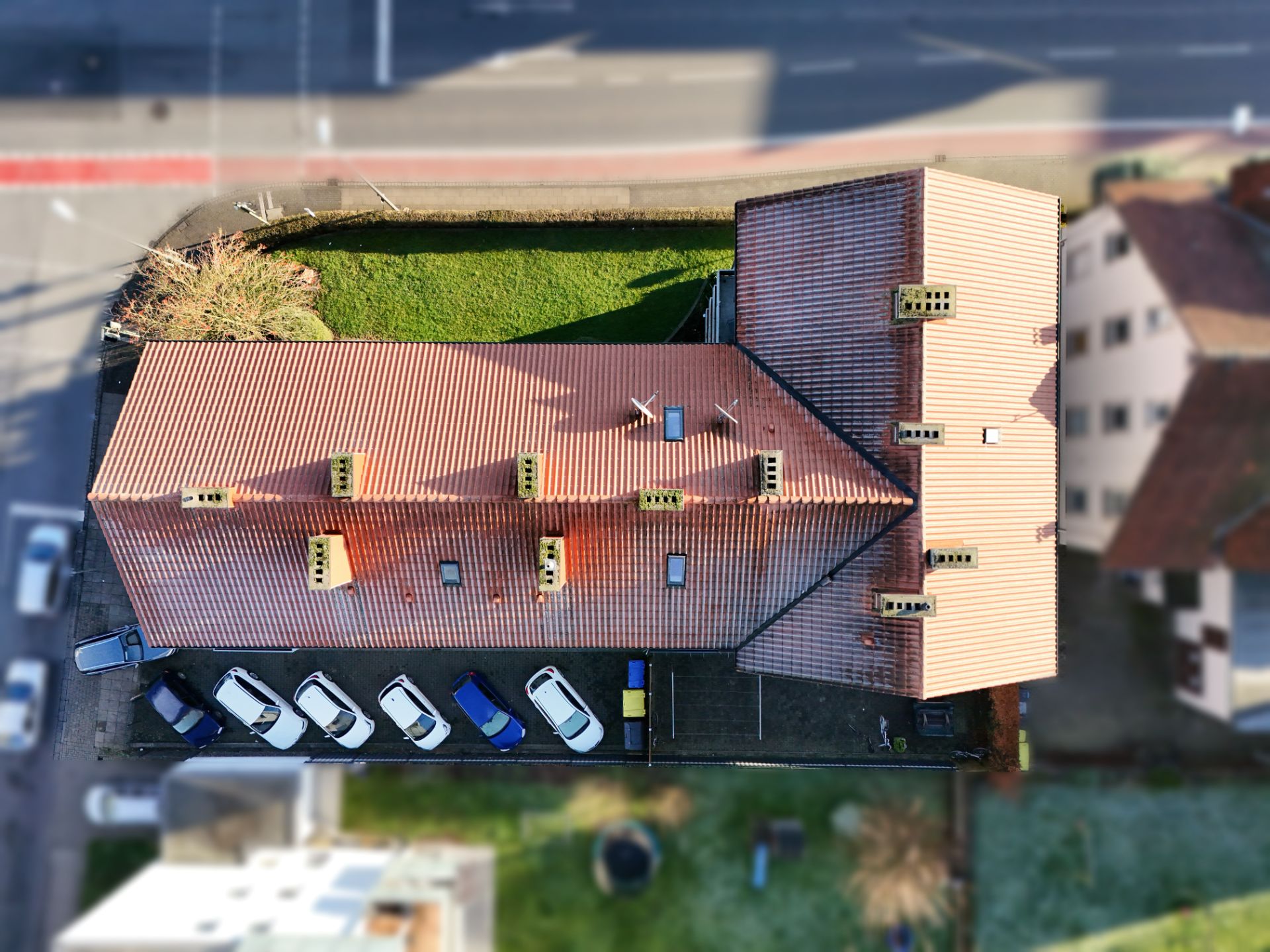 Luftaufnahme eines Wohnhauses mit rotem Dach und mehreren geparkten Autos davor.