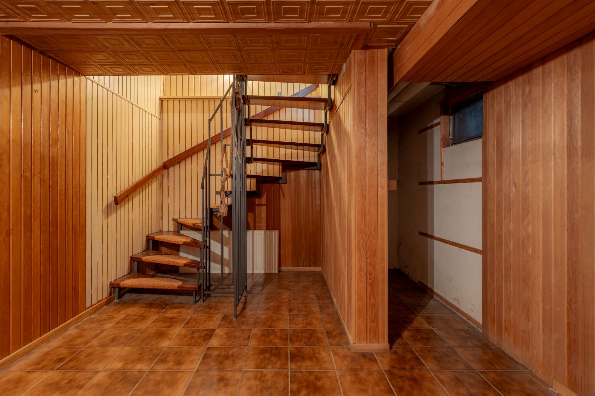 Kellerraum mit Holzvertäfelung, Fliesenboden und Wendeltreppe aus Metall und Holz.