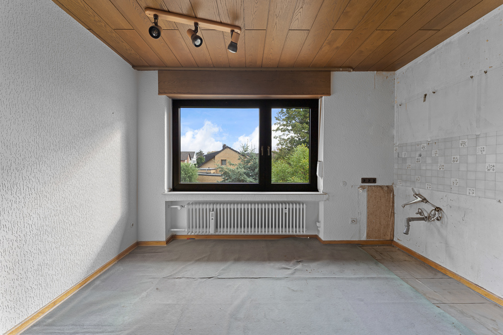 Leerer Raum mit großem Fenster, Holzdecke und Heizkörper unter dem Fenster.