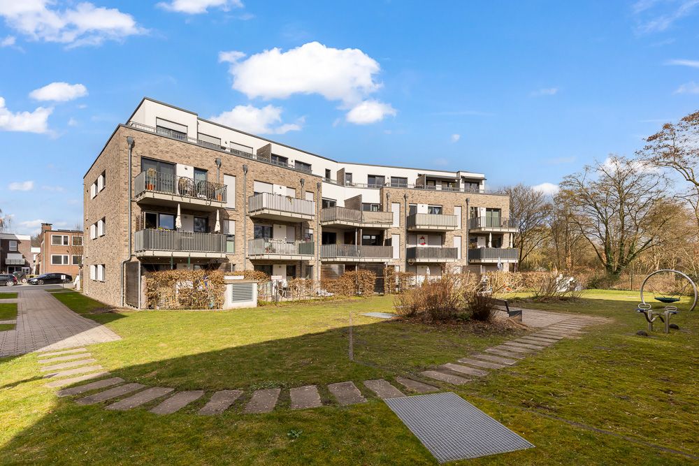 Mehrfamilienhaus mit Balkonen und großem Gartenbereich bei sonnigem Wetter.