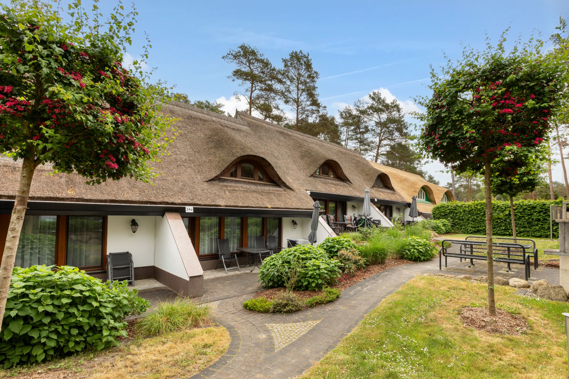 Reihenhaus mit Reetdach, Terrassen, Garten und Bäumen im Vordergrund.