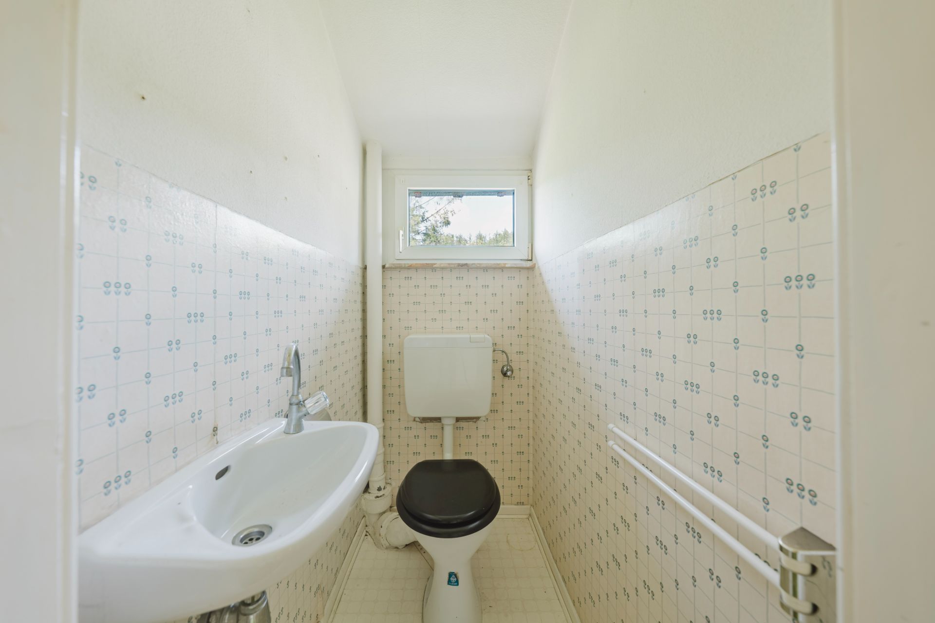 Schmales Badezimmer mit Waschbecken, Toilette und kleinem Fenster.