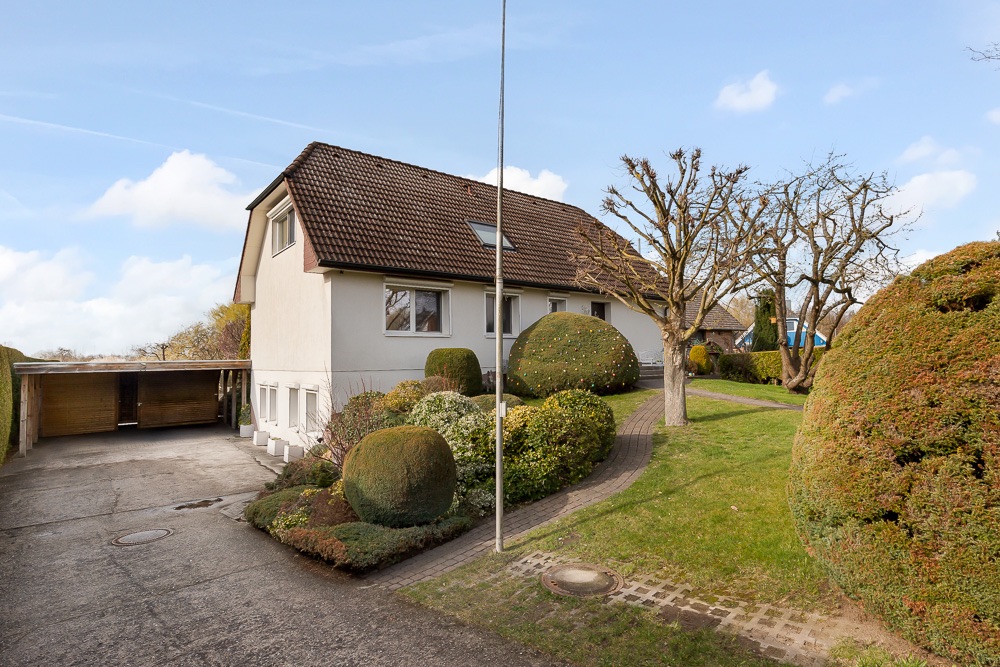 Einfamilienhaus mit schrägem Dach, gepflegtem Garten und einem Carport auf der Einfahrt.