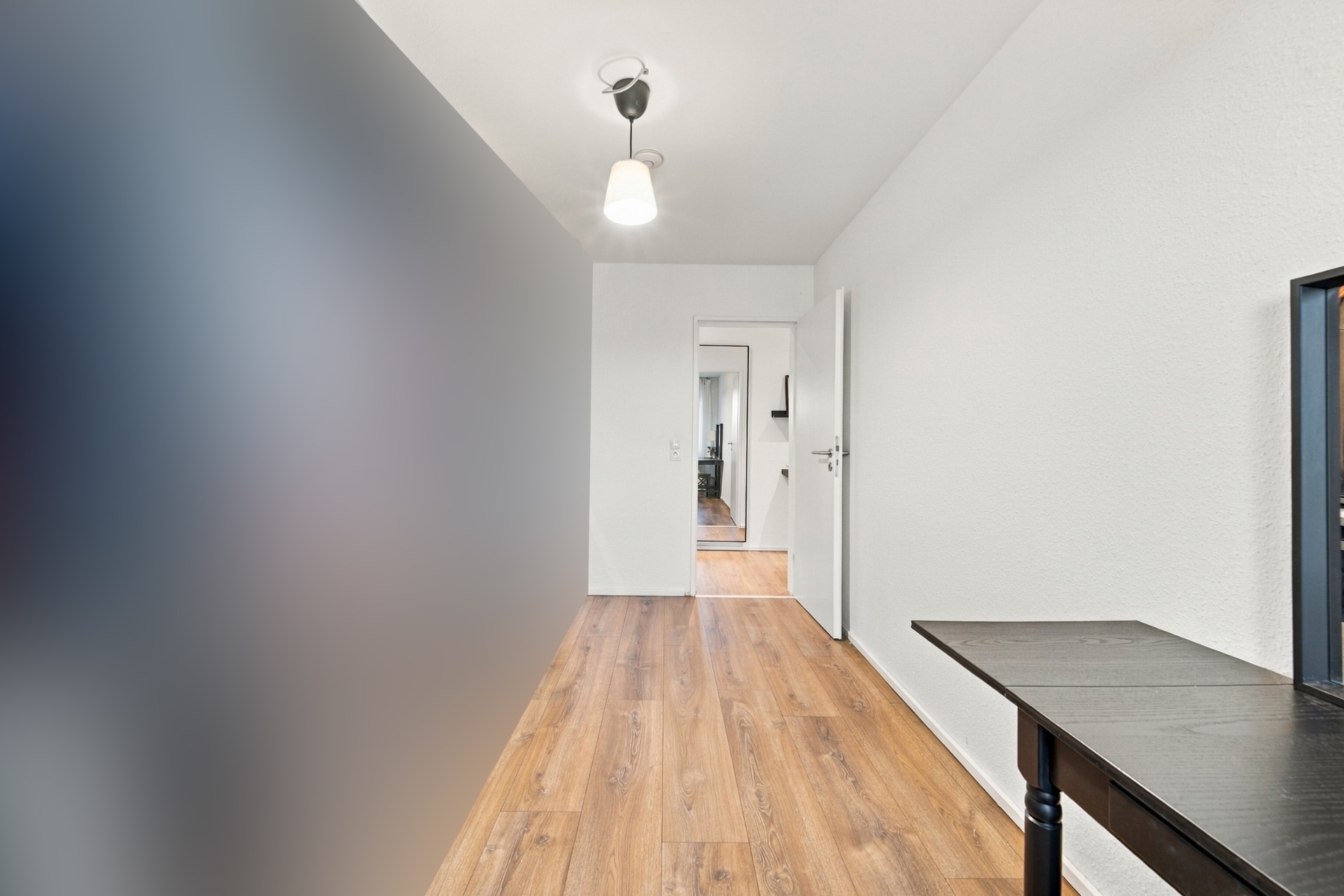 Heller Flur mit Holzboden, weißer Wand und kleiner Tisch am rechten Rand.