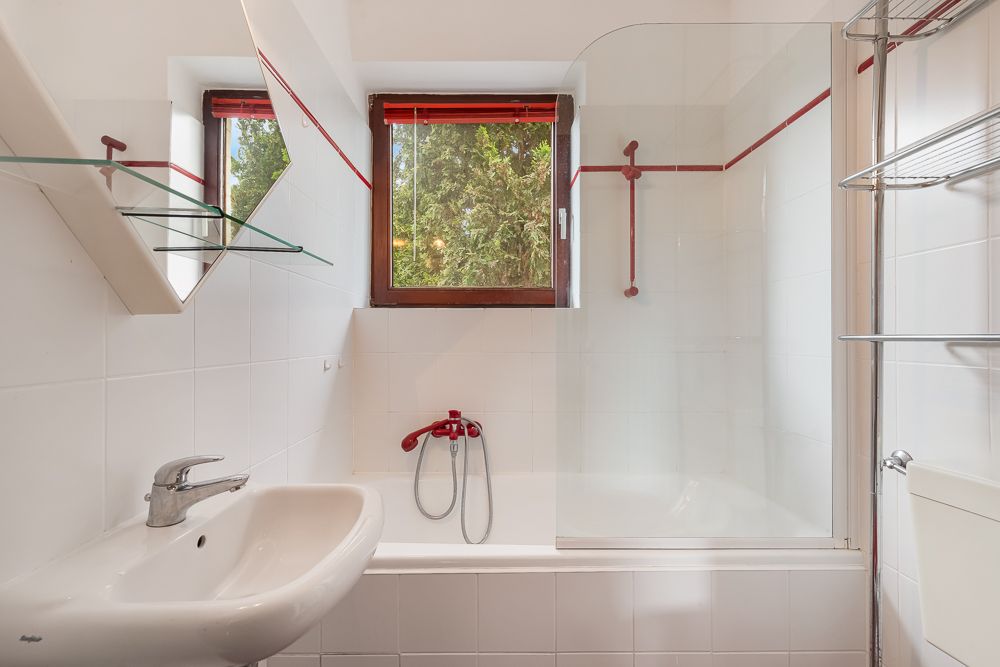 Helles Badezimmer mit Waschbecken, Badewanne, Fenster und Glasregalen an der Wand.