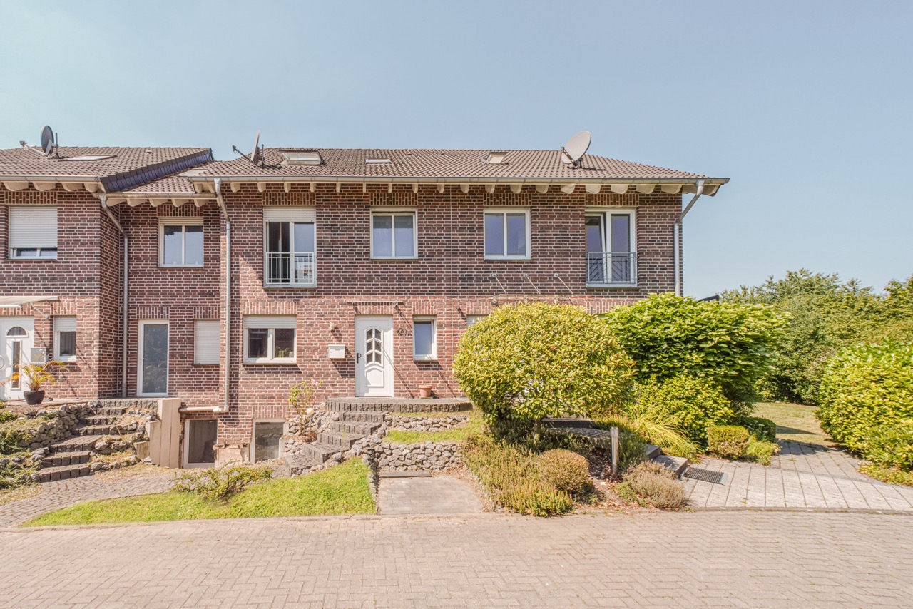 Zweistöckiges Backstein-Reihenhaus mit weißen Fenstern, weißer Tür und Vorgarten.