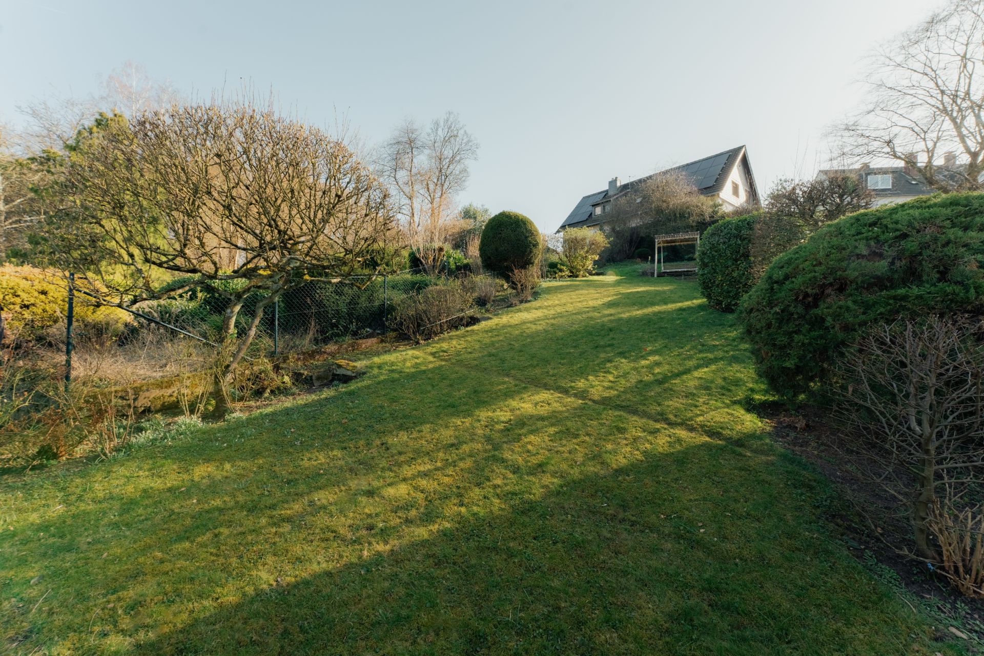 Ein Haus mit großem Garten, Rasenfläche und verschiedenen Büschen und Bäumen.