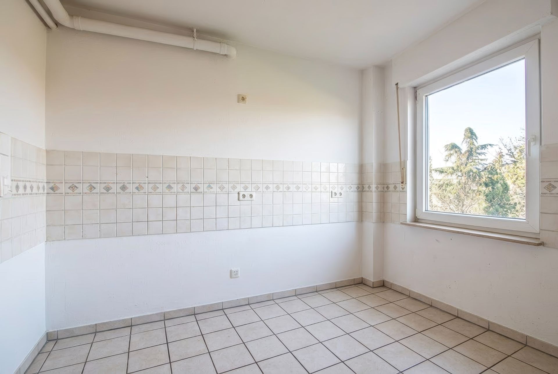 Leerer, gefliester Raum mit weiß gefliesten Wänden und großem Fenster mit Blick ins Grüne.