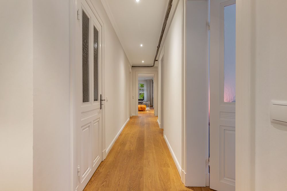 Langer, heller Flur mit Holzboden und weißen Türen in einer Wohnung.