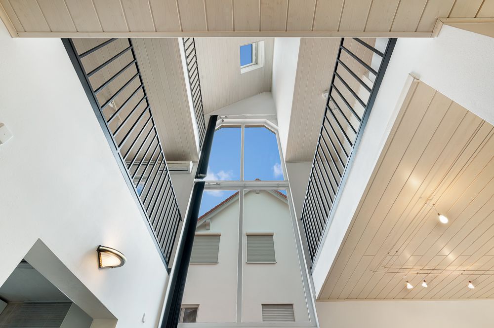 Blick von unten auf ein offenes Treppenhaus mit Geländern und großem Fenster nach außen.