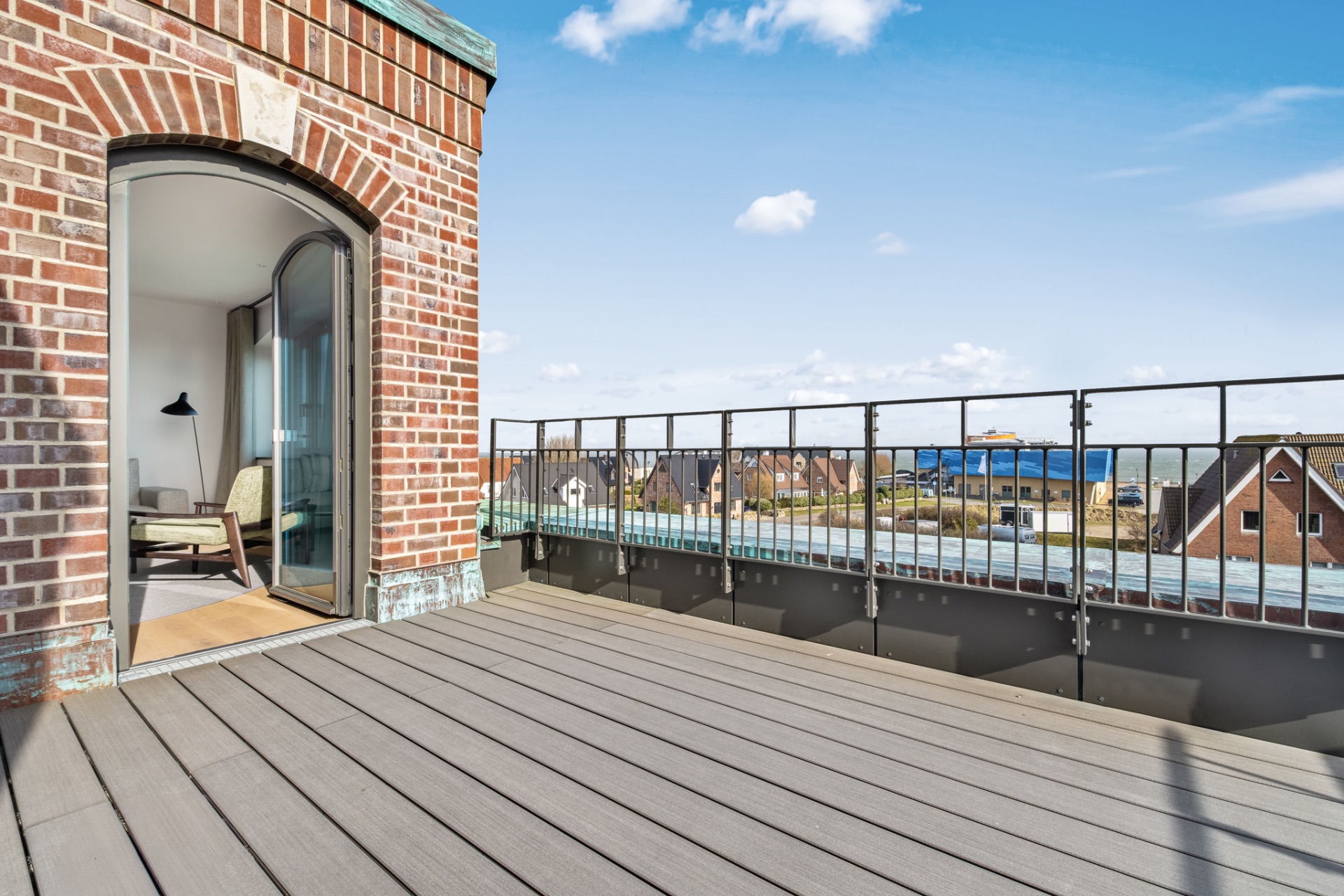 Große Dachterrasse mit Holzfußboden, Backsteinwand und Blick auf Dächer und das Meer.