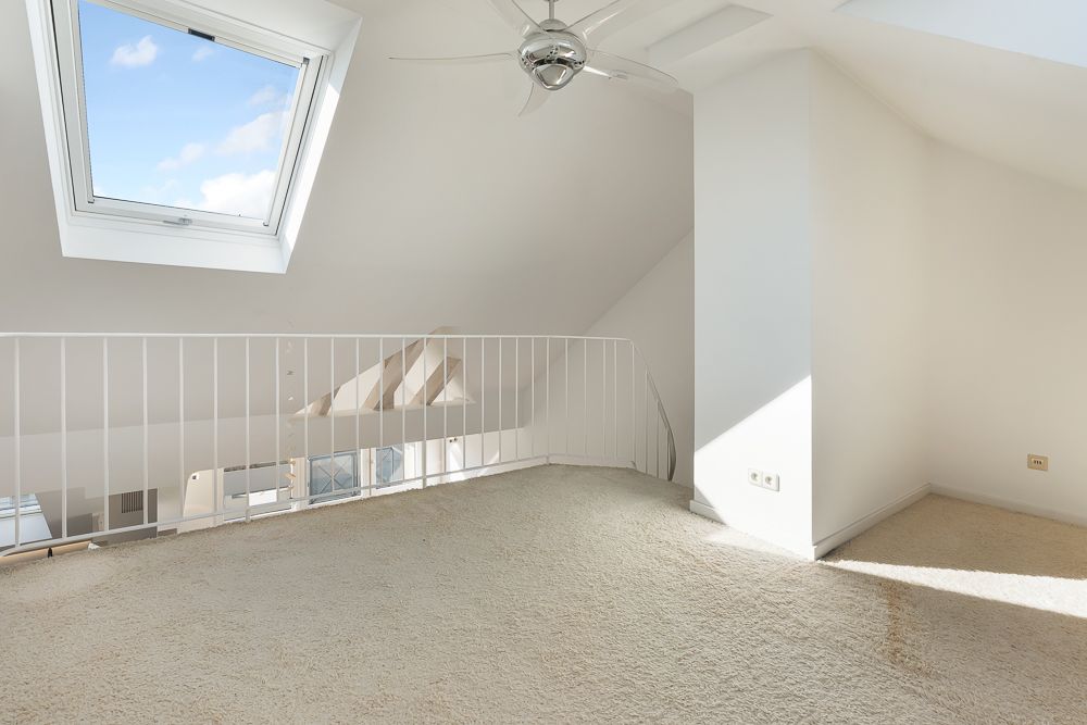 Heller Dachgeschossraum mit Teppich, Dachfenster, Deckenventilator und Geländer.