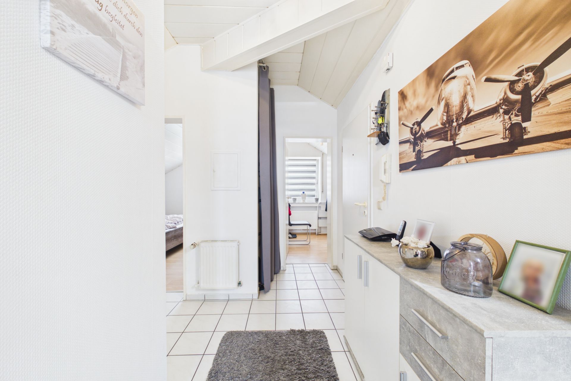 Heller Flur mit Fliesenboden, Sideboard und großem Flugzeugbild an der Wand.