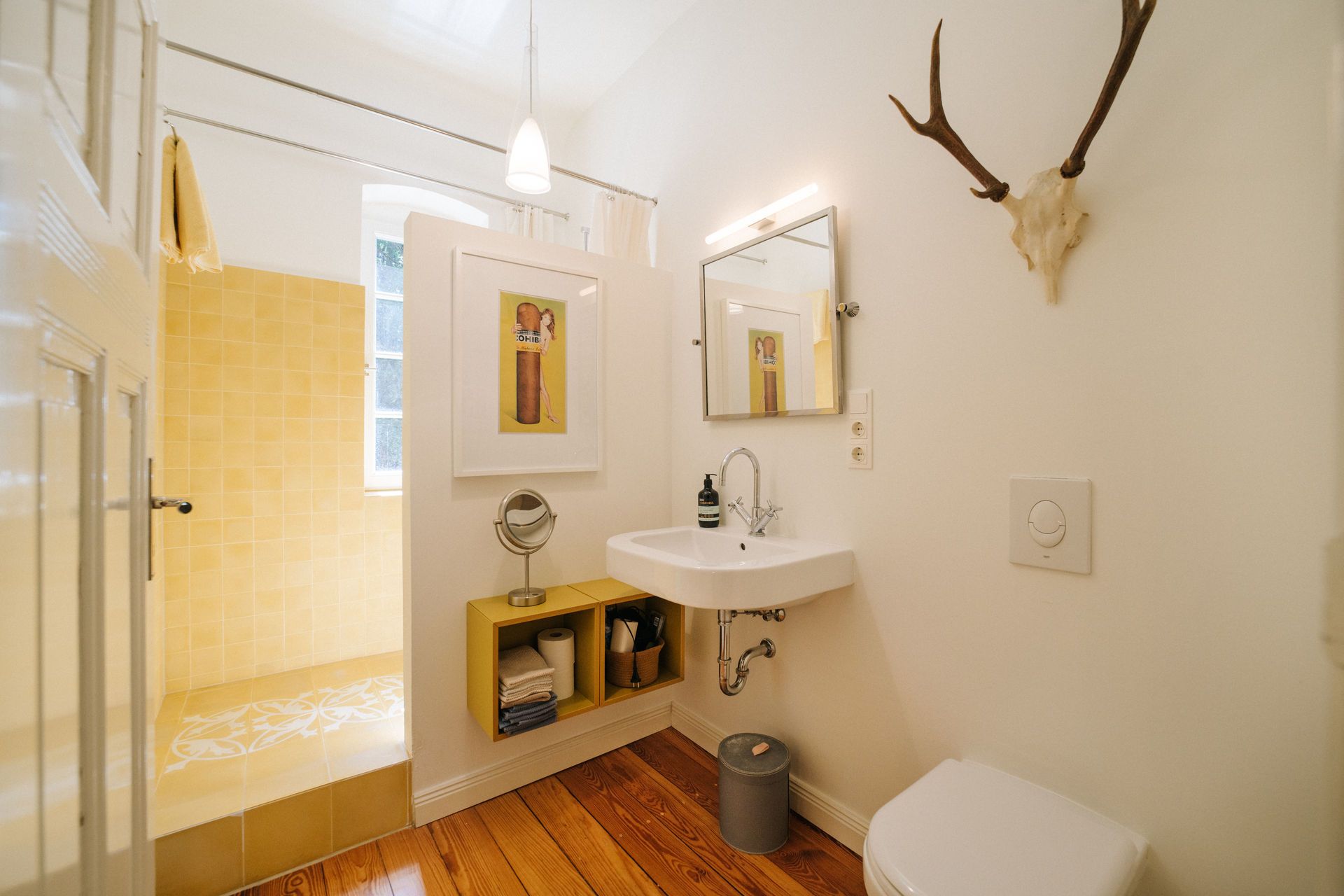 Helles Badezimmer mit Dusche, Waschbecken, Spiegel, WC und Hirschgeweih an der Wand.