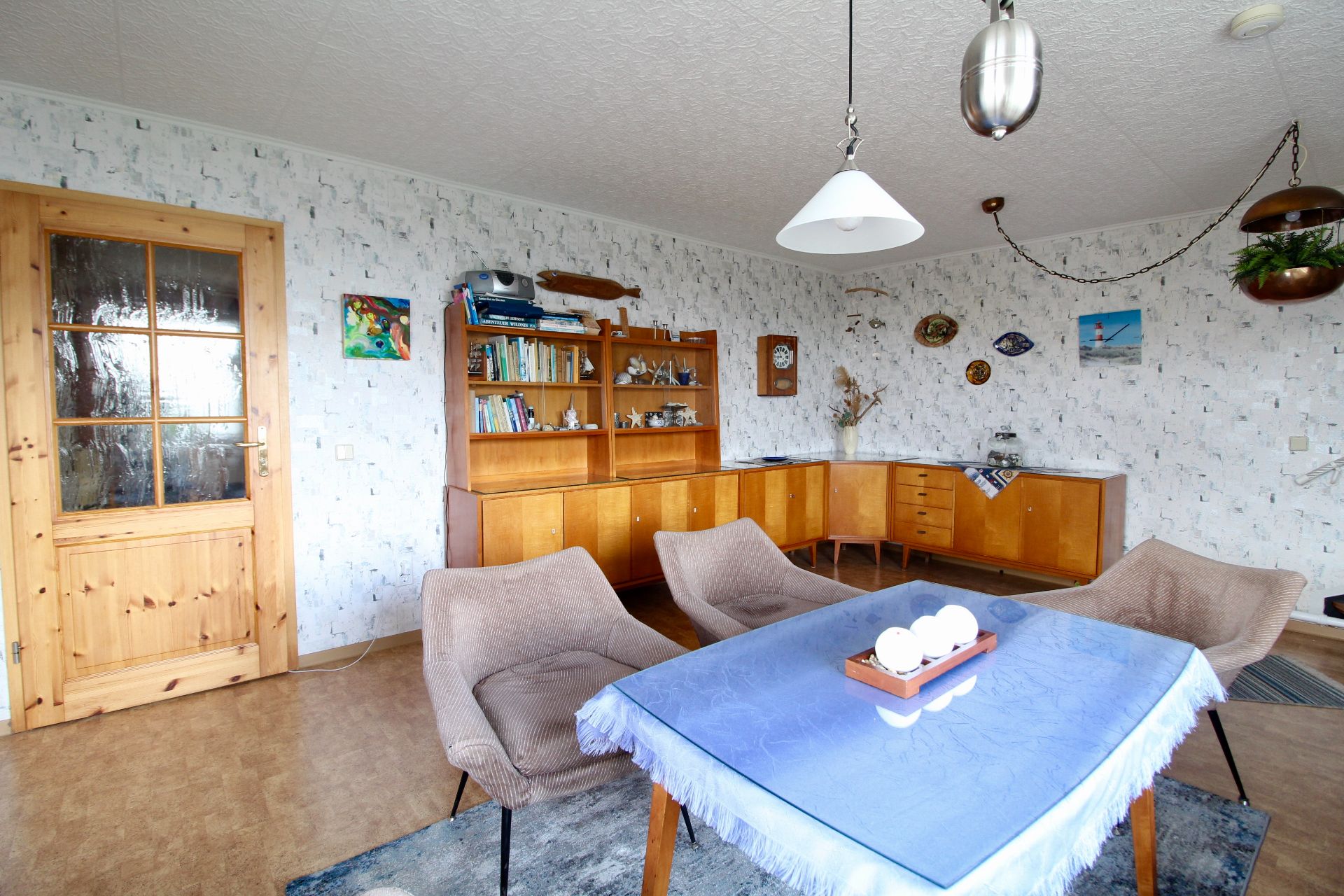 Wohnzimmer mit Esstisch, vier Stühlen, Holzschrank und Dekoration an den Wänden.