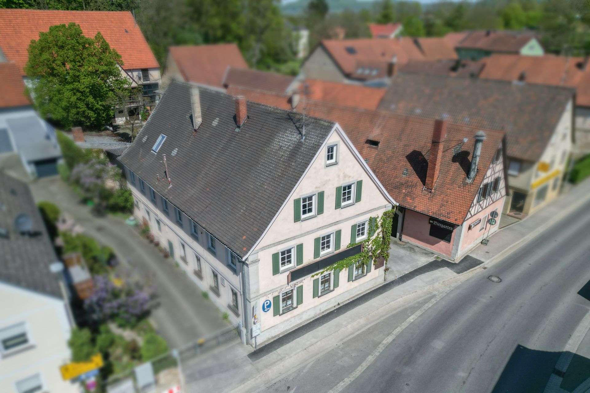 Zweistöckiges Wohnhaus mit Satteldach und weißen Fensterläden an einer Straßenkreuzung.