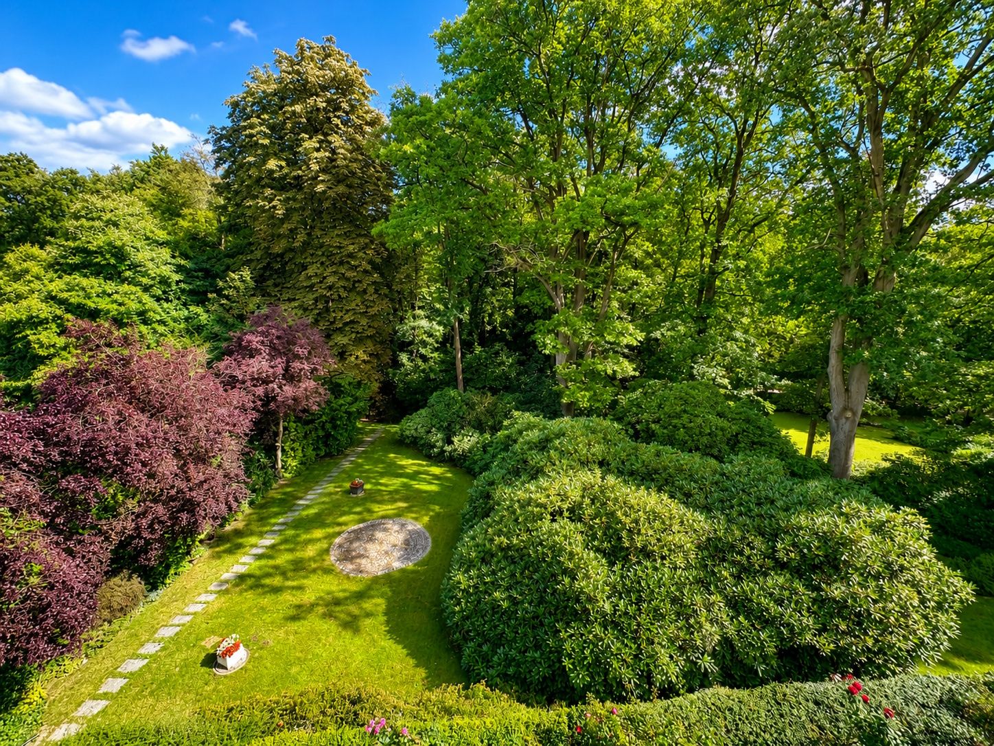 Großer Garten mit Rasen, Büschen, Bäumen und einem runden Kiesbereich in der Mitte.