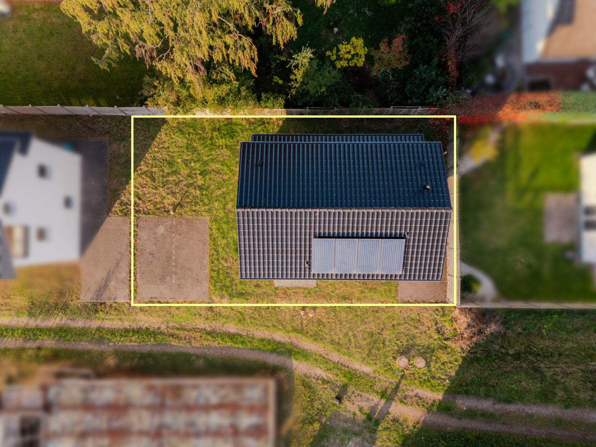 Luftaufnahme eines Hauses mit dunklem Dach und Solarpanel, umgeben von Garten.