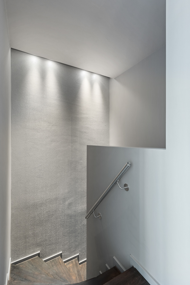 Moderne, enge Treppe mit Holzstufen, silbernem Handlauf und Wandbeleuchtung.