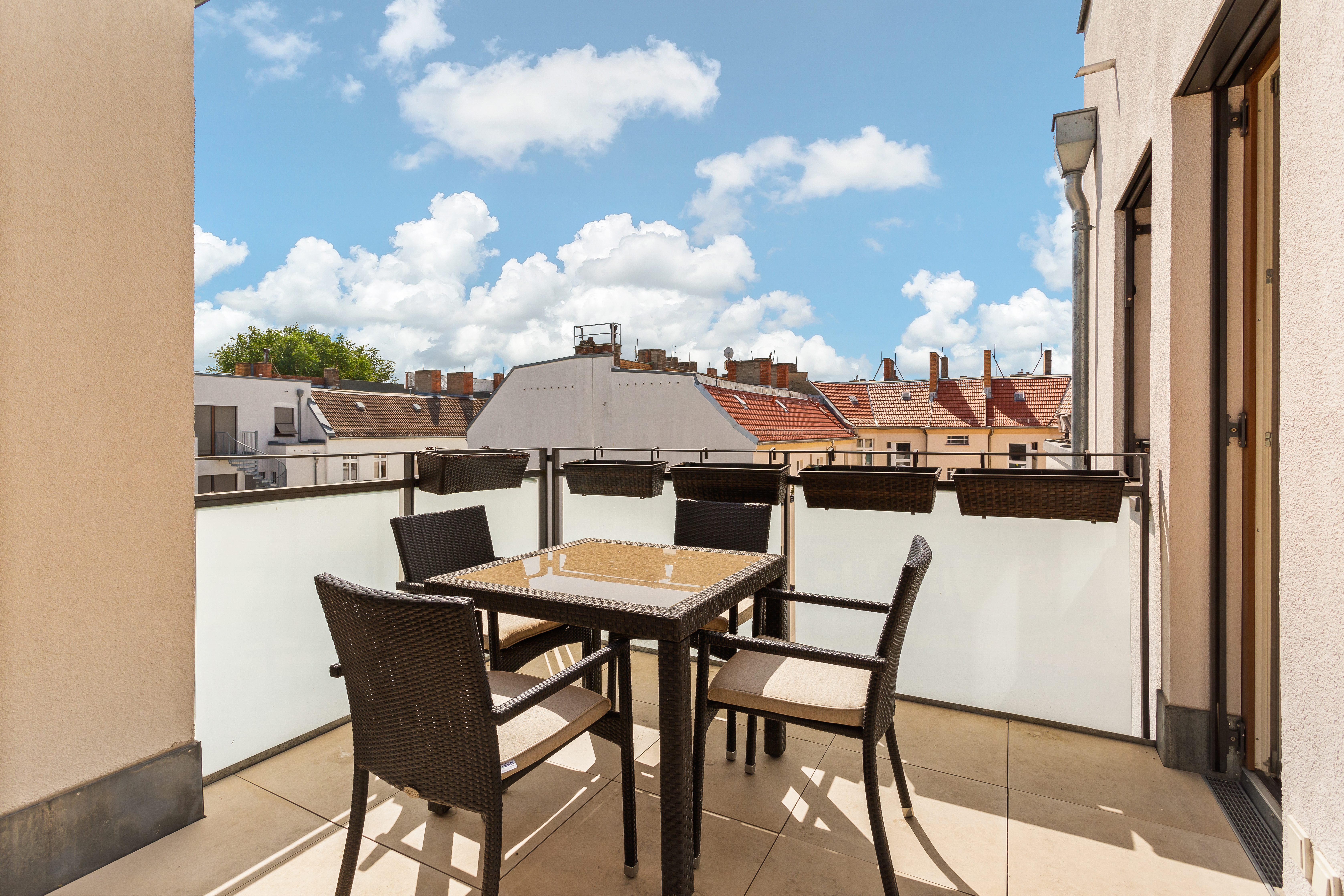 Möblierter Balkon mit vier Stühlen und Tisch, Blick auf Dächer und blauen Himmel.