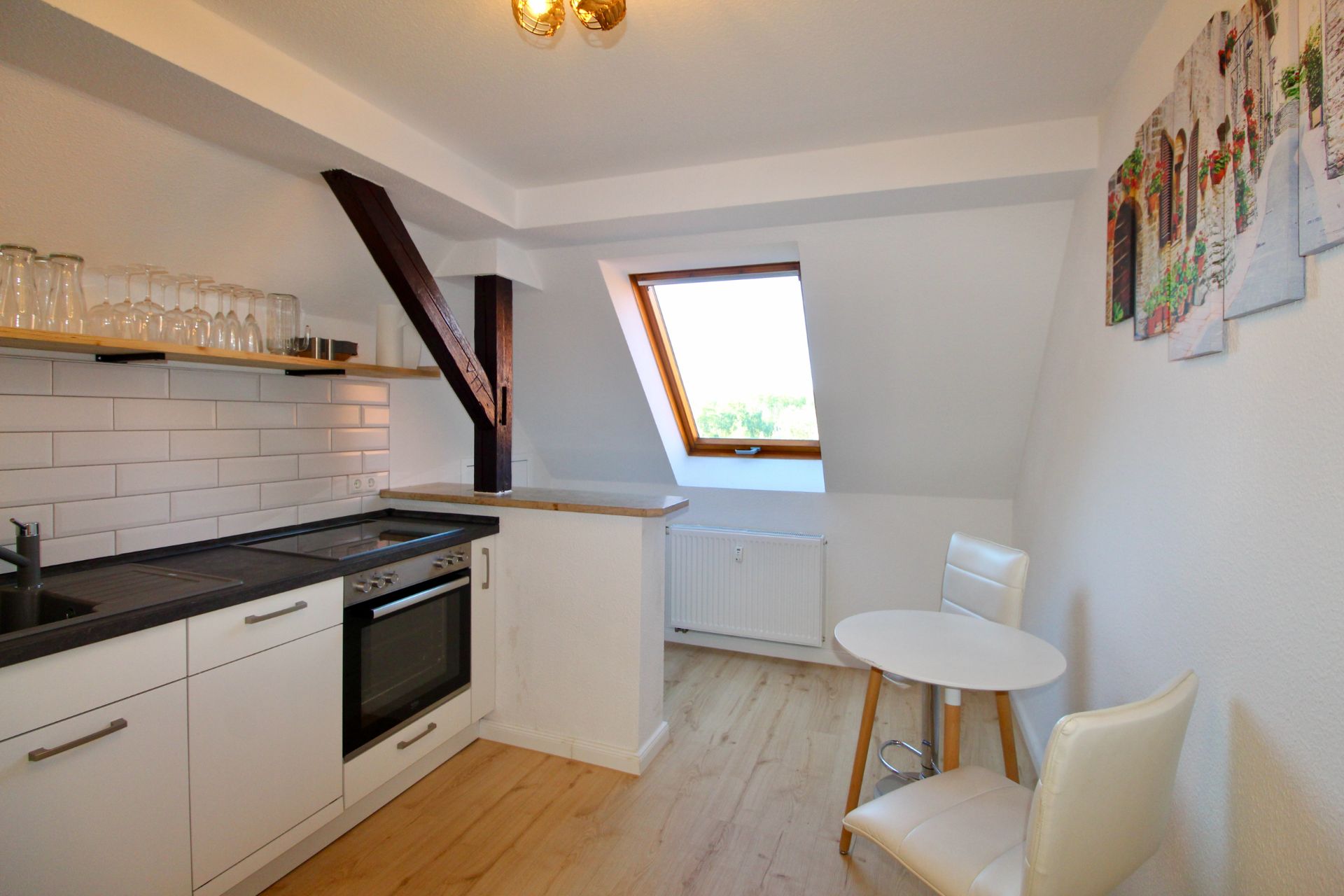 Helle Küche mit Dachfenster, Esstisch und zwei weißen Stühlen auf Holzfußboden.