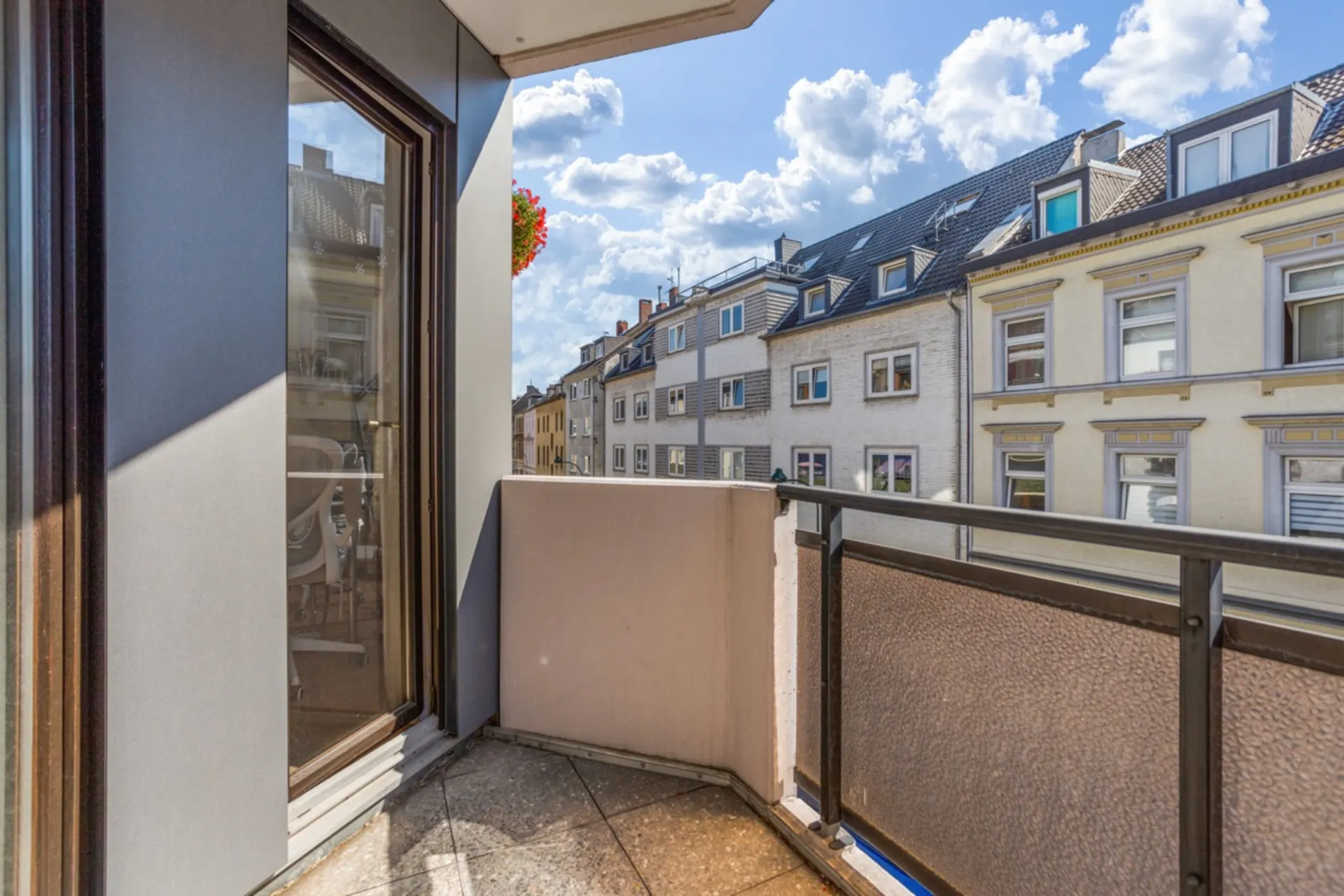 Balkon mit Glasgeländer und Blick auf Nachbarhäuser an einem sonnigen Tag.