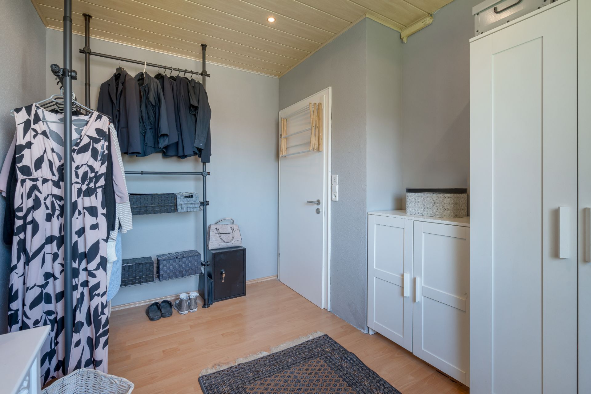 Helles Ankleidezimmer mit Garderobenstange, Schränken und Kleidung.