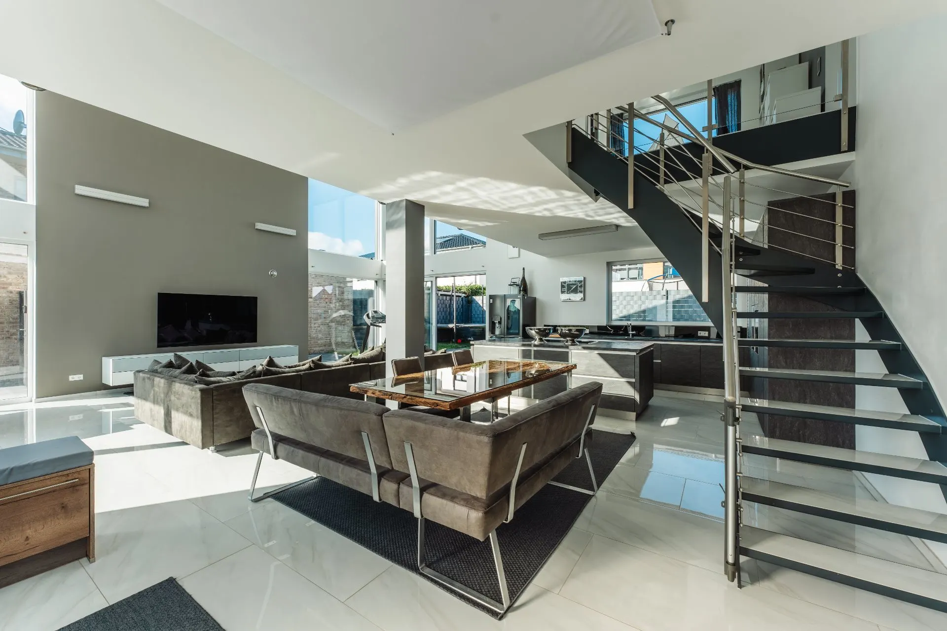 Modernes Wohnzimmer mit großen Fenstern, Sofas, Esstisch und Treppe.