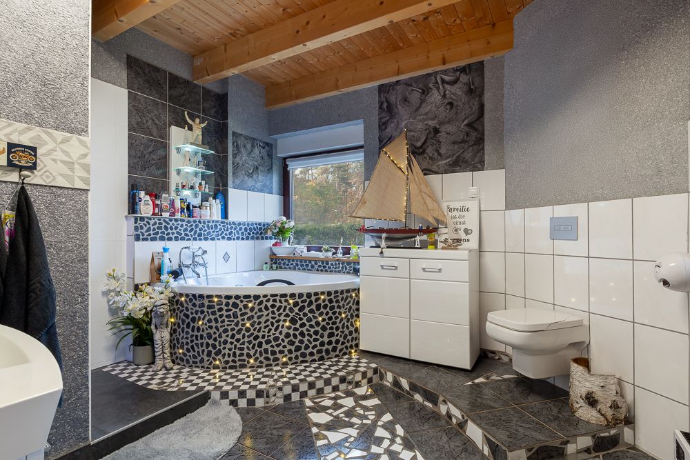 Modernes Badezimmer mit gemusterter Badewanne, weißem Schrank und schwebender Toilette.