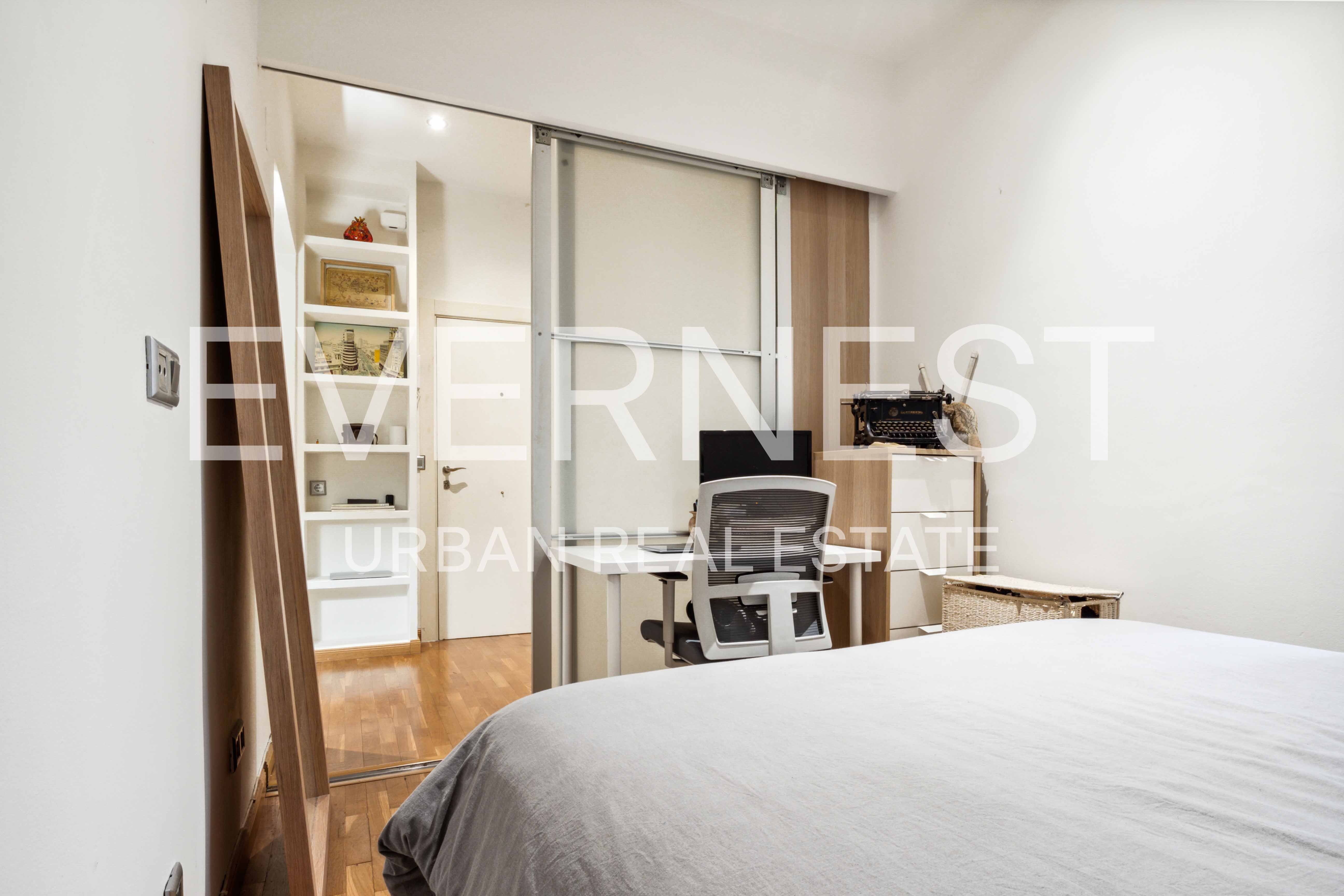 Schlafzimmer mit Bett, Schreibtisch, Stuhl und Regal mit Dekoration auf Holzfußboden.
