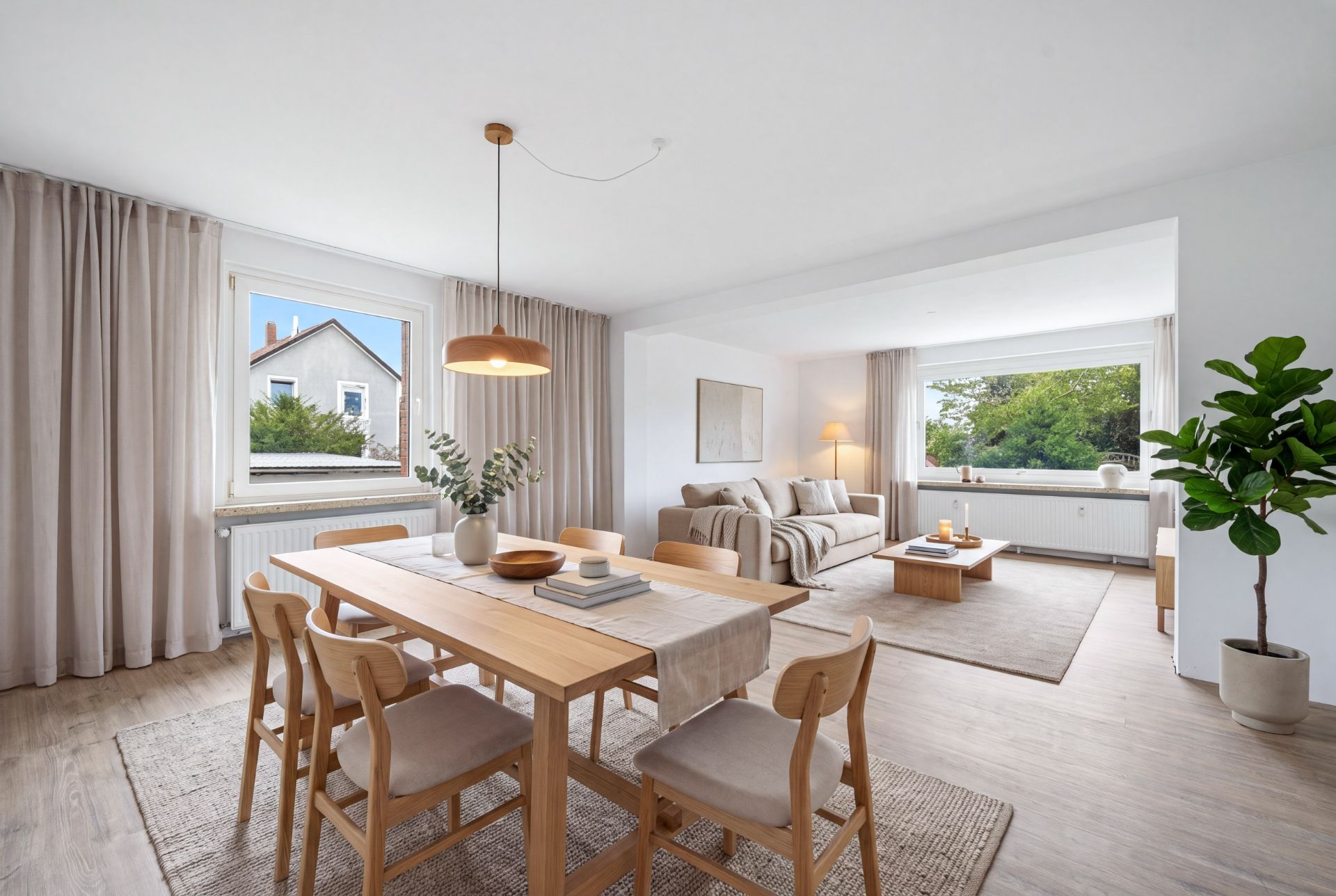 Helles Wohnzimmer mit Essbereich, Holztisch, gemütlichem Sofa und großer Zimmerpflanze.
