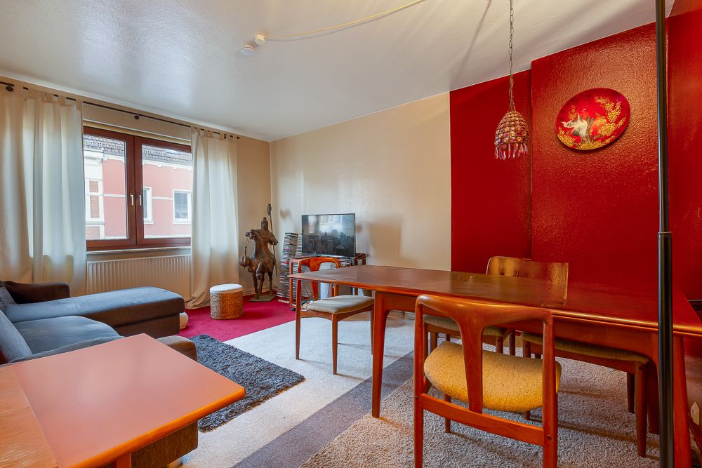 Wohnzimmer mit Ecksofa, Esstisch, Stühlen, Fernseher und roter Akzentwand.